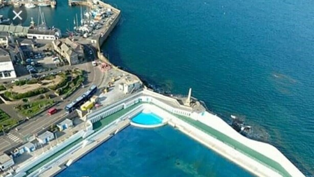 Vue a érienne d’une zone côtière avec une grande piscine de forme irrégulière, entourée d’une barrière blanche.