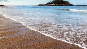 Une plage de galets, des vagues et, au loin, une île sur laquelle se trouve un bâtiment.
