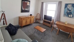 Un salon moderne comprenant un canapé, une table à manger en bois, un téléviseur et un trépied.