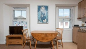 Un coin repas avec une table et des chaises en bois, un téléviseur posé sur un meuble et un tableau accroché au mur.