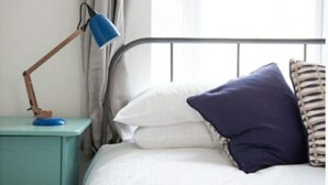 Un lit avec des oreillers blancs et bleu foncé, une lampe de bureau bleue et une table de chevet turquoise.