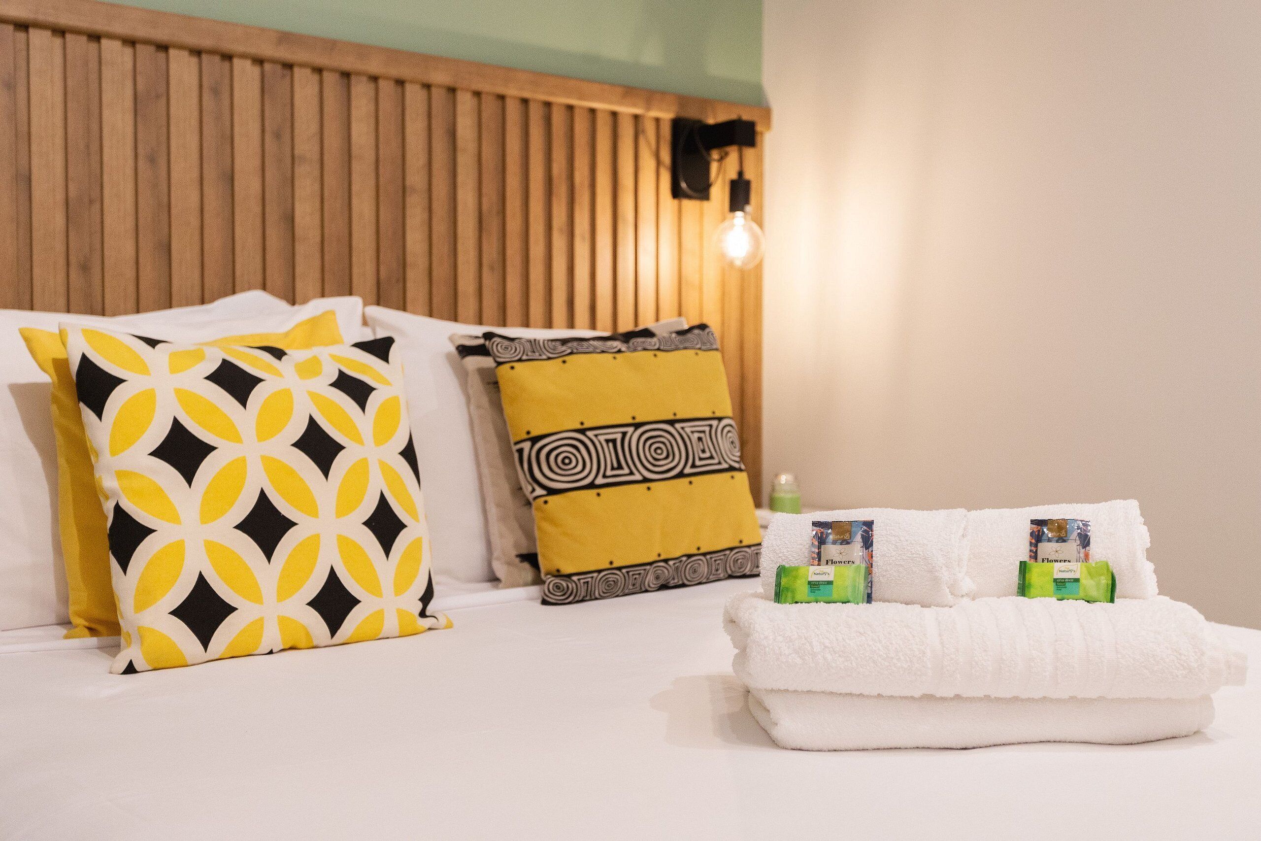 A neatly made bed with patterned pillows, a white towel, and toiletries.