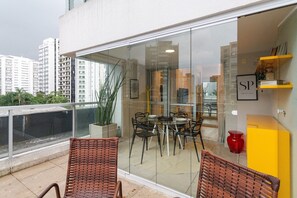 A balcony with wicker chairs, a glass table, and a yellow cabinet. - Wish Moema 15 (São Paulo)