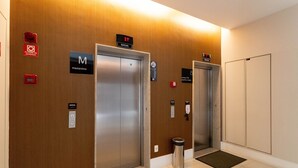 An elevator area with two elevators, a fire alarm, and a trash bin. - Wish Moema 15 (São Paulo)