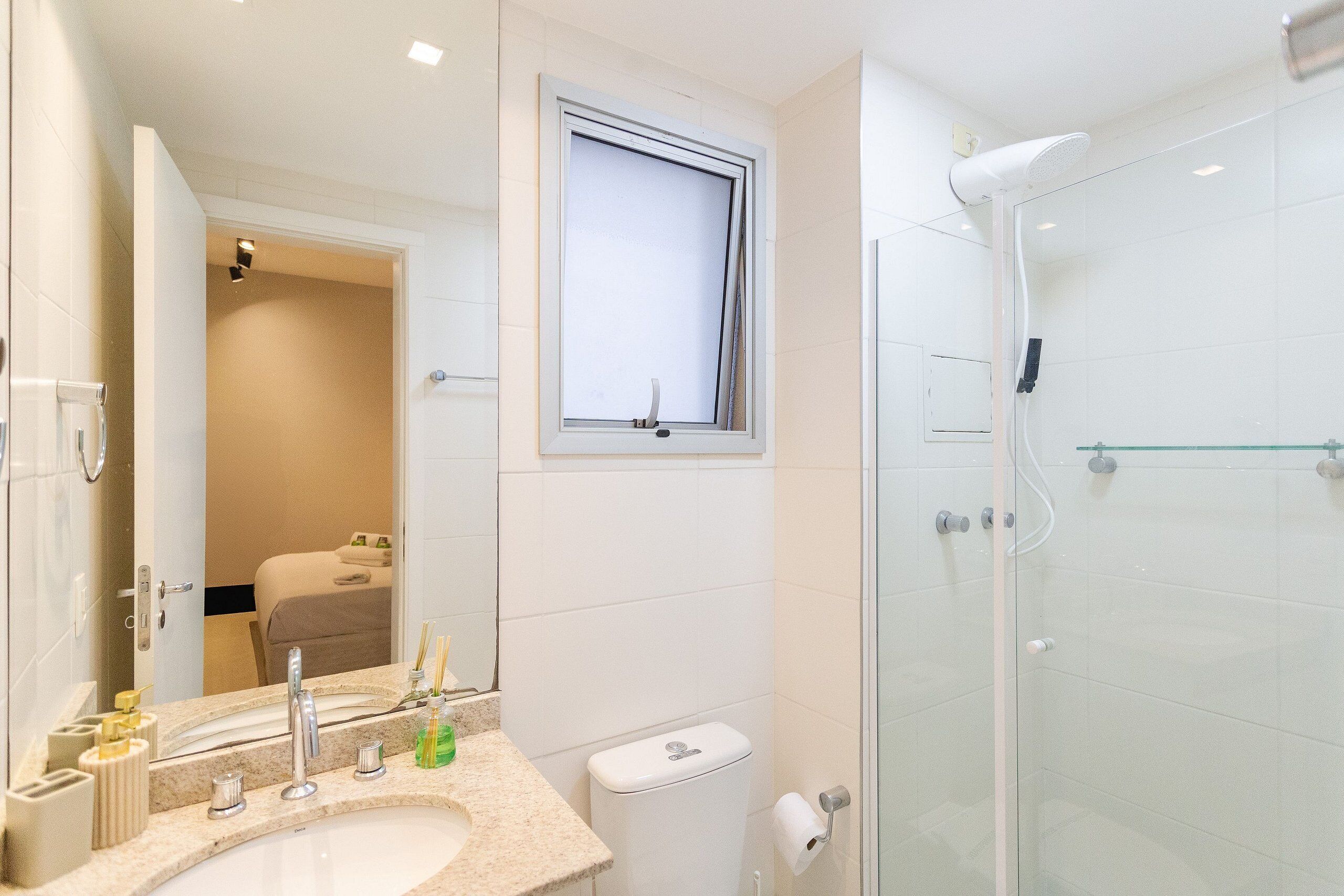 A modern bathroom with a large mirror, a sink, a toilet, and a glass-enclosed shower.