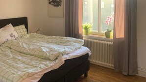 A bedroom with a bed, a window with curtains, a radiator, and a hanging light fixture.