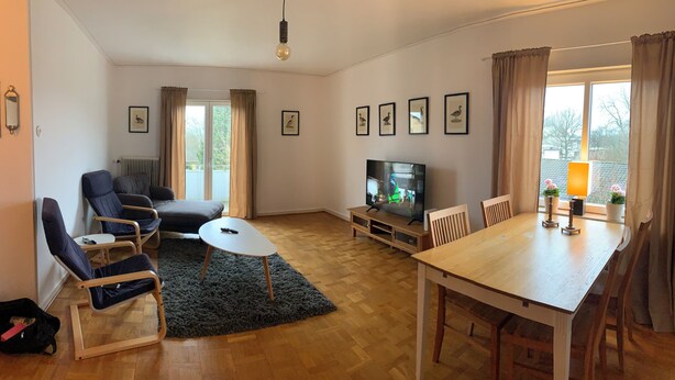 A living room with a sofa, chairs, a TV, a dining table, and a view of the outdoors.