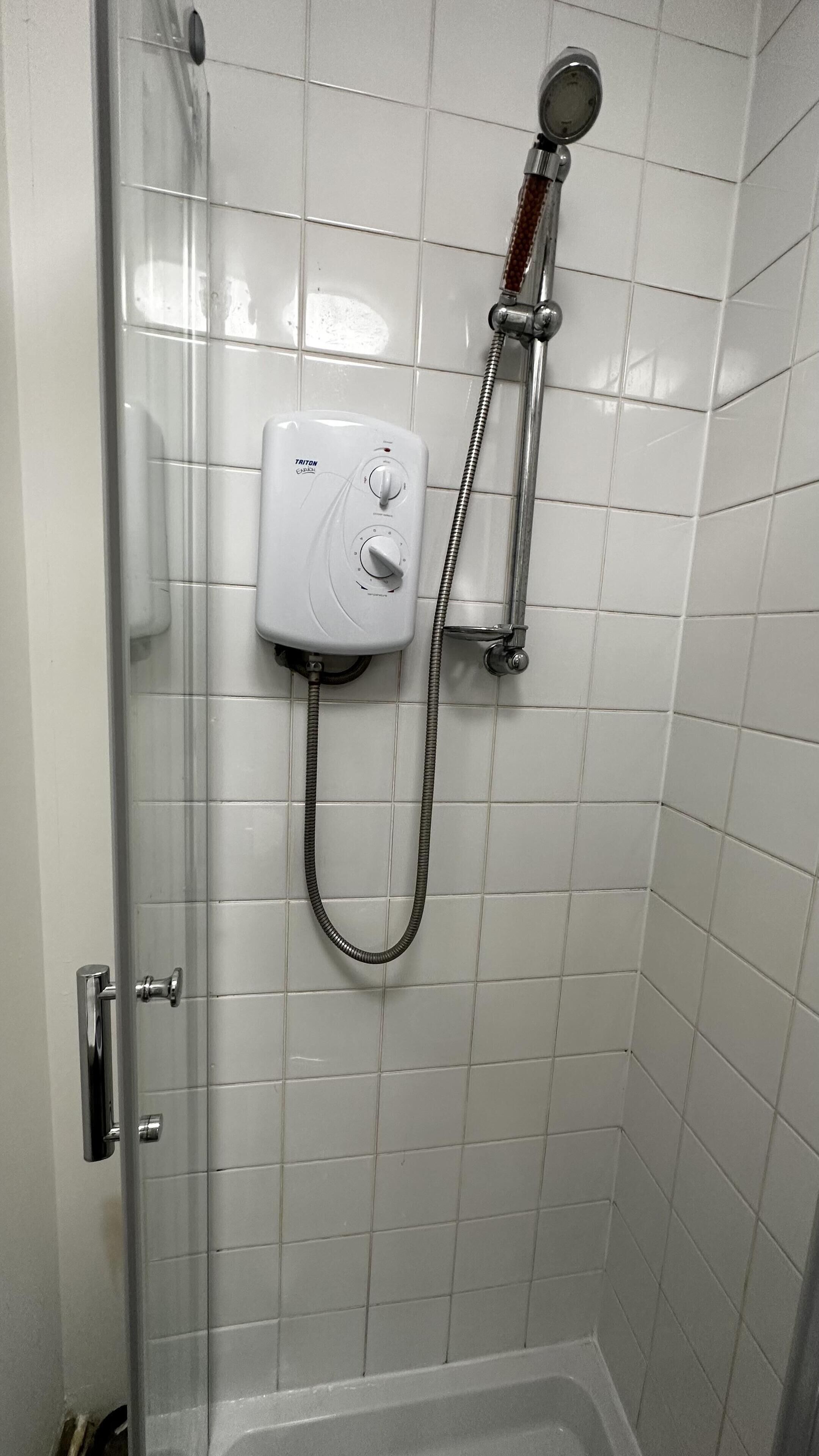 A shower with a control panel, a handheld showerhead, and a flexible hose.