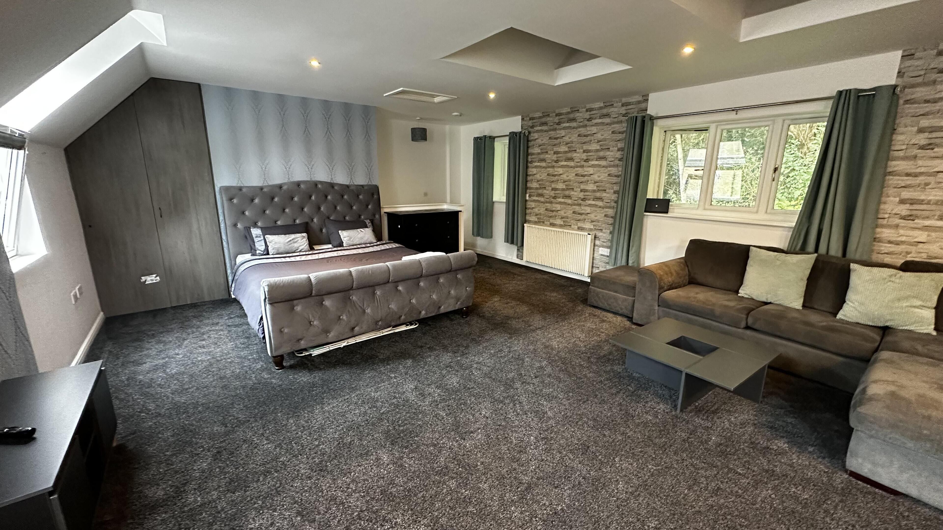 A modern hotel room with a large bed, a sofa, a coffee table, and a TV.