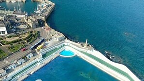 Vista aérea de una marina costera con una piscina grande y de forma peculiar rodeada por una barrera blanca.