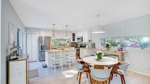A modern kitchen with white cabinetry, stainless steel appliances, and a dining area with a round table and chairs. - Contemporary home close to beaches with private pool, open floorplan, and... (East Quogue)