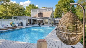 A swimming pool with lounge chairs, a hanging chair, and a barbecue area. - Contemporary home close to beaches with private pool, open floorplan, and... (East Quogue)