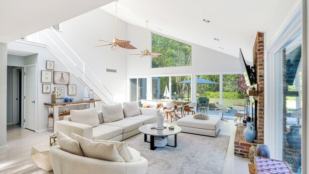 A spacious living room with a high ceiling, a large window overlooking a garden, and a staircase leading to an upper level. - Contemporary home close to beaches with private pool, open floorplan, and... (East Quogue)