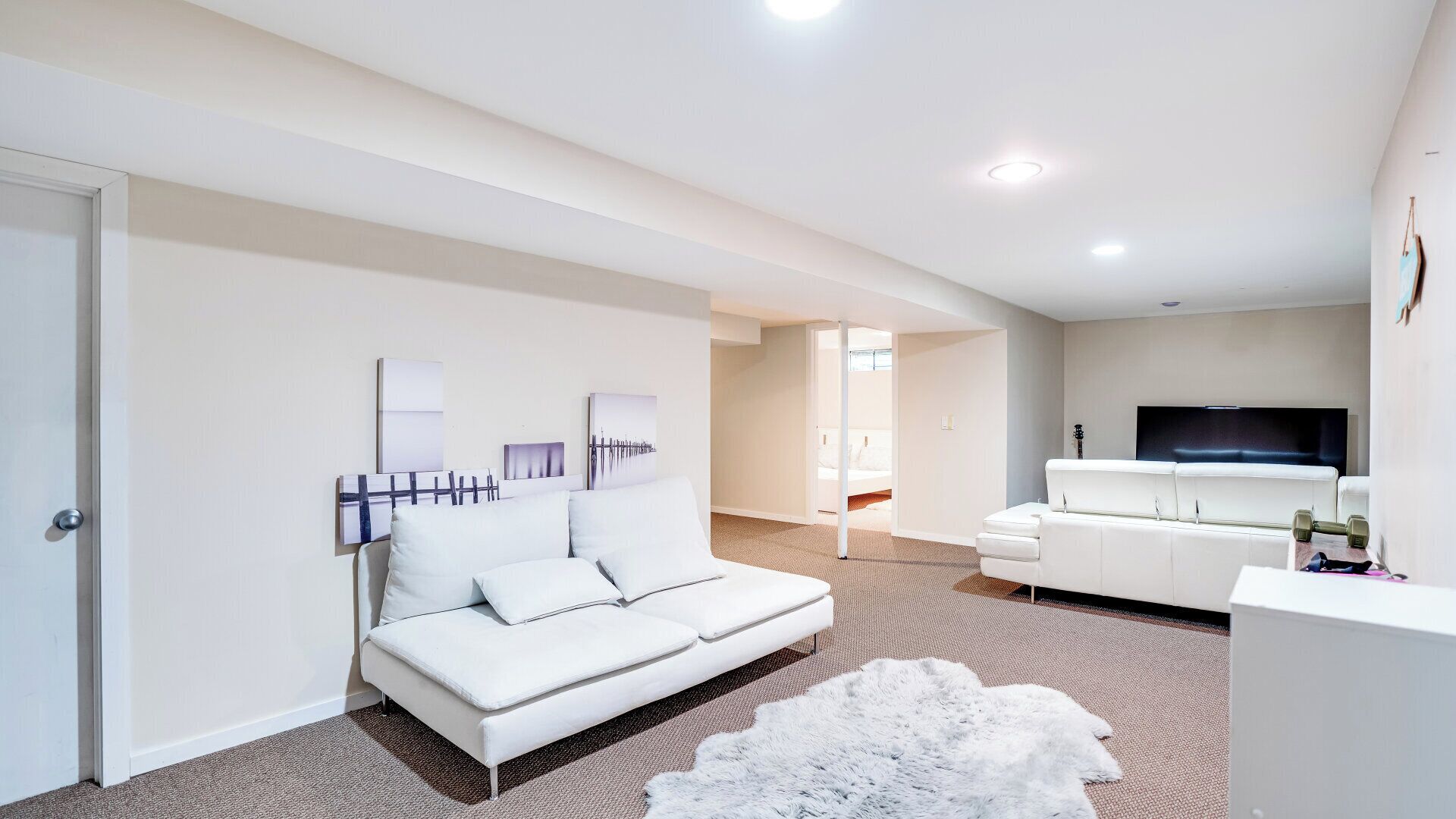 A modern, well-lit living room with a white sofa, a flat-screen TV, and a white cabinet.