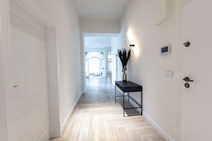 A hallway with a light wooden floor, a black console table with a vase, and a wall-mounted light fixture.