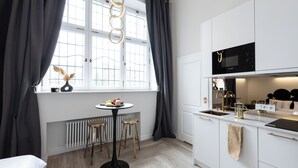 A modern kitchen with white cabinets, a black microwave, and a round dining table with stools. - Srebrna Luxury Apartments (Lodz)