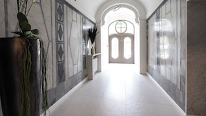 A hallway with marble walls, a large potted plant, and a double door at the end. - Srebrna Luxury Apartments (Lodz)