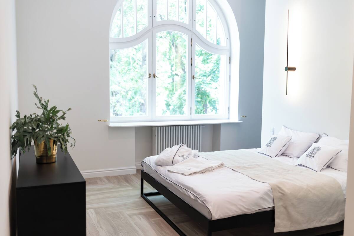Une chambre à coucher avec un lit, un radiateur, une fenêtre et une plante.