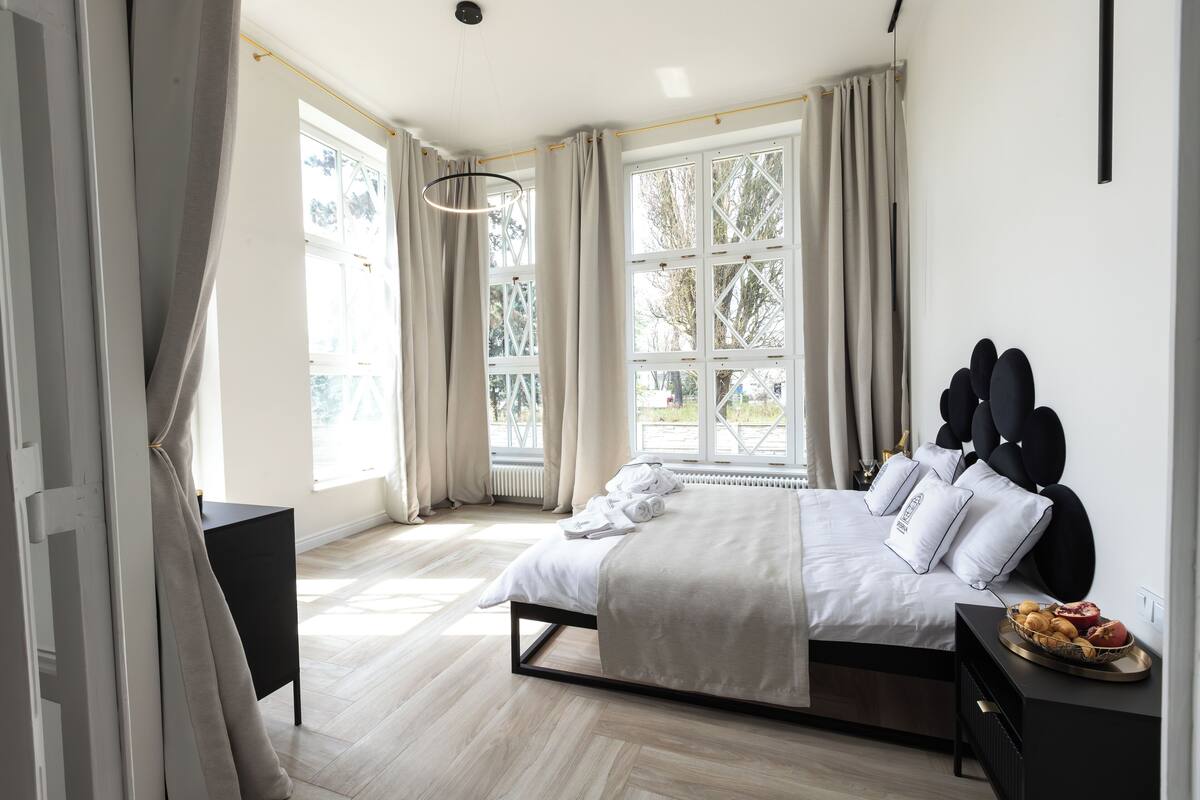 Une chambre à coucher moderne, avec un lit, une table de chevet et une vue sur l’extérieur grâce à de grandes fenêtres.