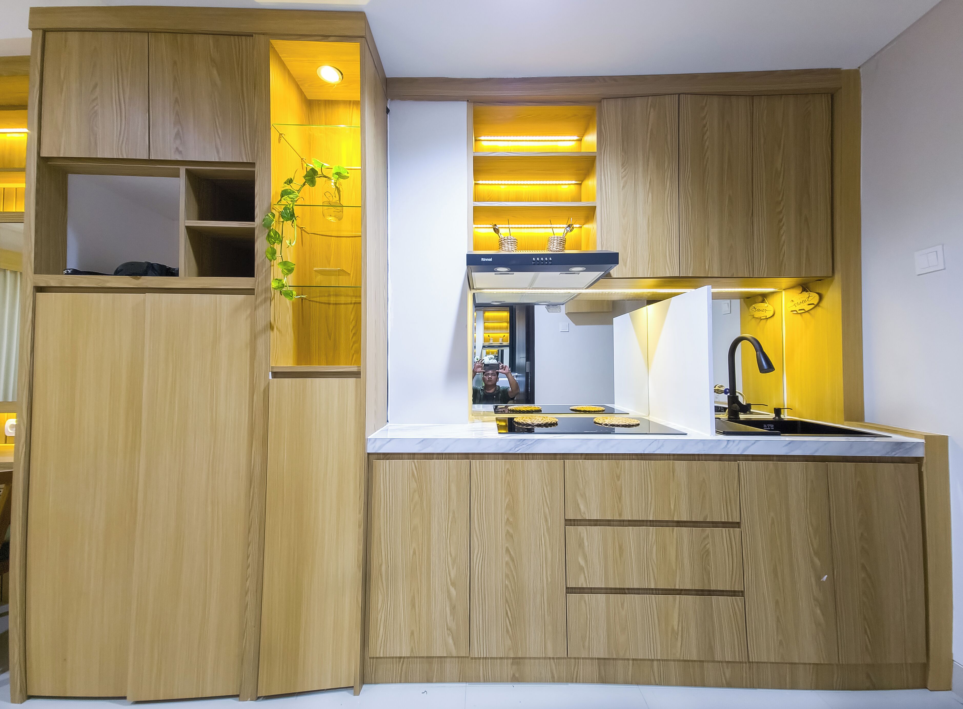 A compact kitchen with wooden cabinetry, a built-in sink, and under-cabinet lighting.