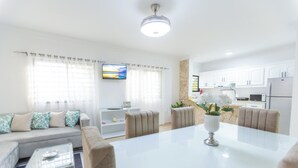 A modern living room with a sofa, coffee table, and dining table. There is a kitchen area with cabinets and appliances visible. - Puerto Plata (Puerto Plata)
