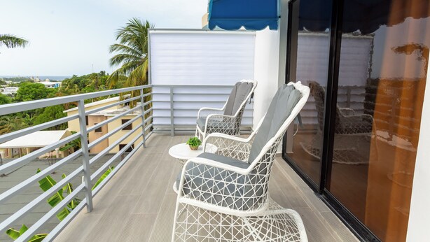 A balcony with white wicker chairs and a small table, overlooking a cityscape and palm trees. - Puerto Plata (Puerto Plata)