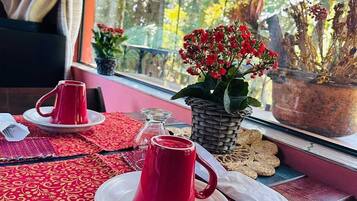 Uma mesa com xícaras e pires vermelhos, uma pequena planta em vaso e uma cesta de vime no parapeito da janela.
