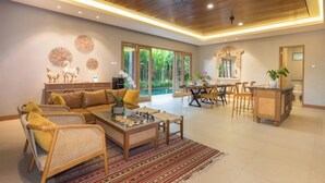 A spacious living area with a wooden ceiling, a sofa set, a coffee table with chess, and a dining area with a wooden table and chairs.
