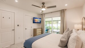 A bedroom with a bed, a ceiling fan, a window with curtains, and a painting on the wall. - Chic Bungalow with Fire Pit, Lanai & Games! (Naples)