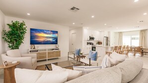 A modern living room with a sofa, coffee table, and a large flat-screen TV. - Chic Bungalow with Fire Pit, Lanai & Games! (Naples)