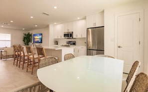 A modern kitchen with white cabinets, stainless steel appliances, and a dining area with a white table and wicker chairs.