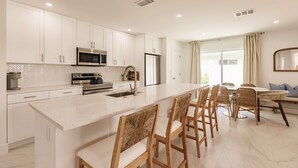A modern kitchen with white cabinets, stainless steel appliances, and a central island with bar stools. - Chic Bungalow with Fire Pit, Lanai & Games! (Naples)