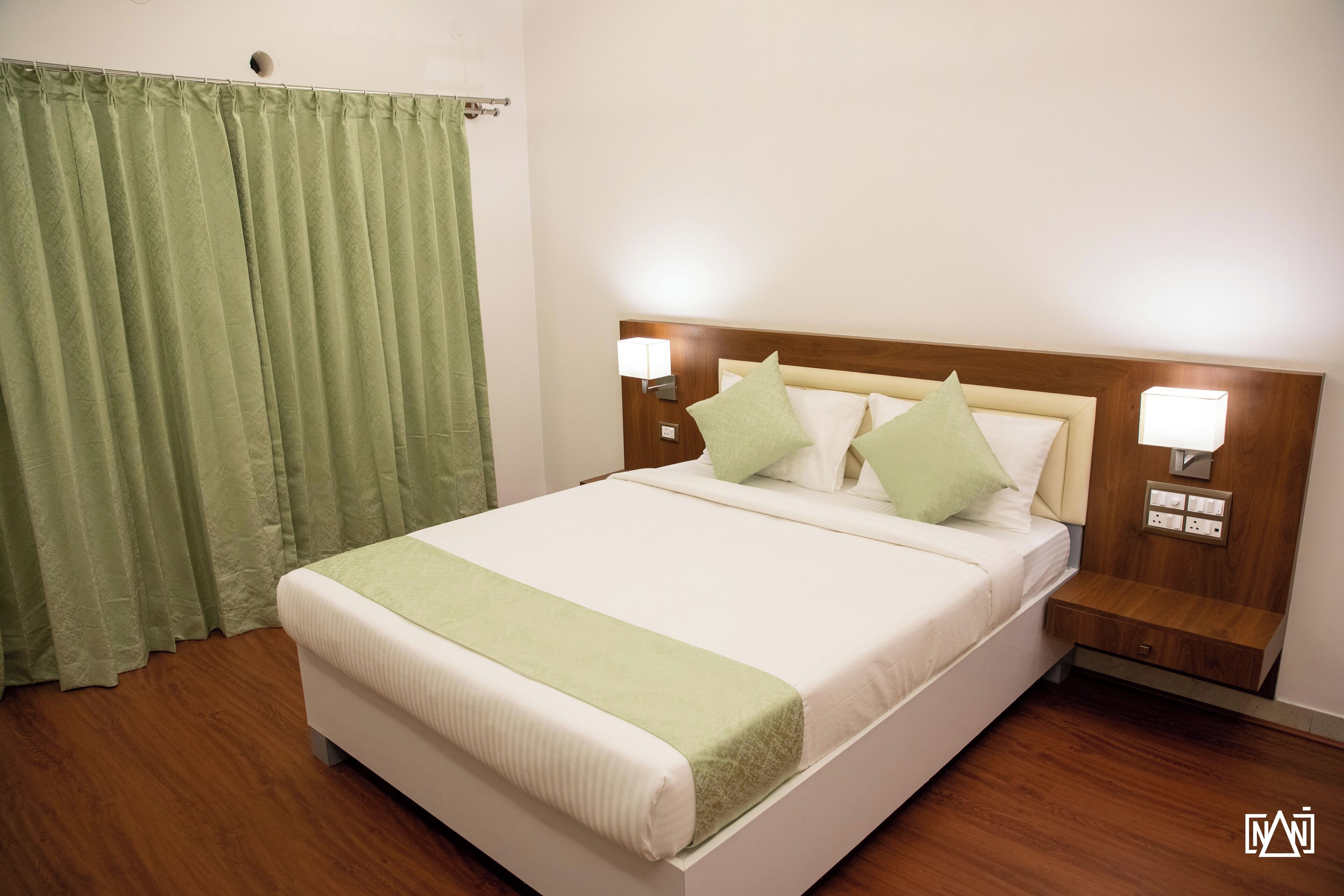 A neatly made bed with a green throw, two bedside lamps, and a wooden nightstand.