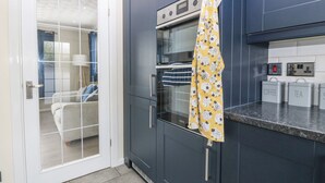 A modern kitchen with dark cabinets, a built-in oven, and a microwave. There are labeled containers for coffee and tea on the counter. - Cynefin (Llangefni)