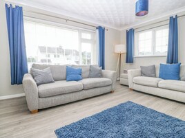 Una sala de estar moderna con dos sofás grises, un tapete azul y ventanas grandes con cortinas azules.