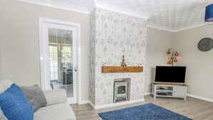 A living room with a sofa, a blue rug, a fireplace, a TV, and a clock on the wall. - Cynefin (Llangefni)