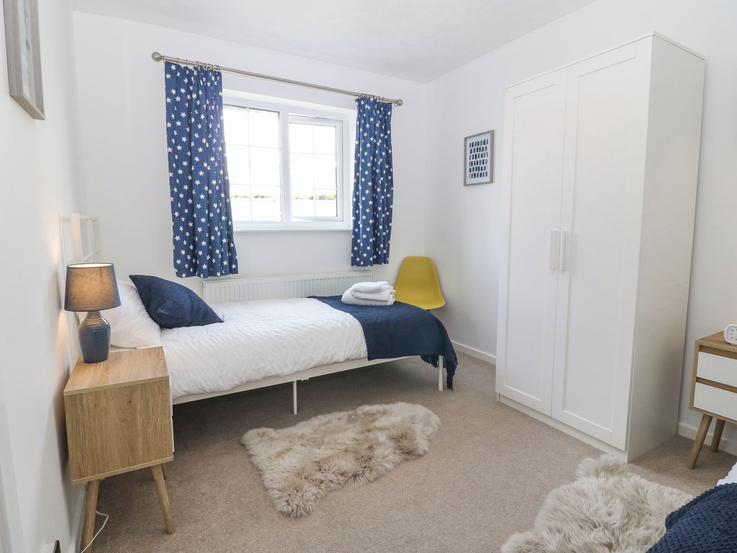 A bedroom with a bed, a nightstand, a wardrobe, a window with curtains, and a rug.