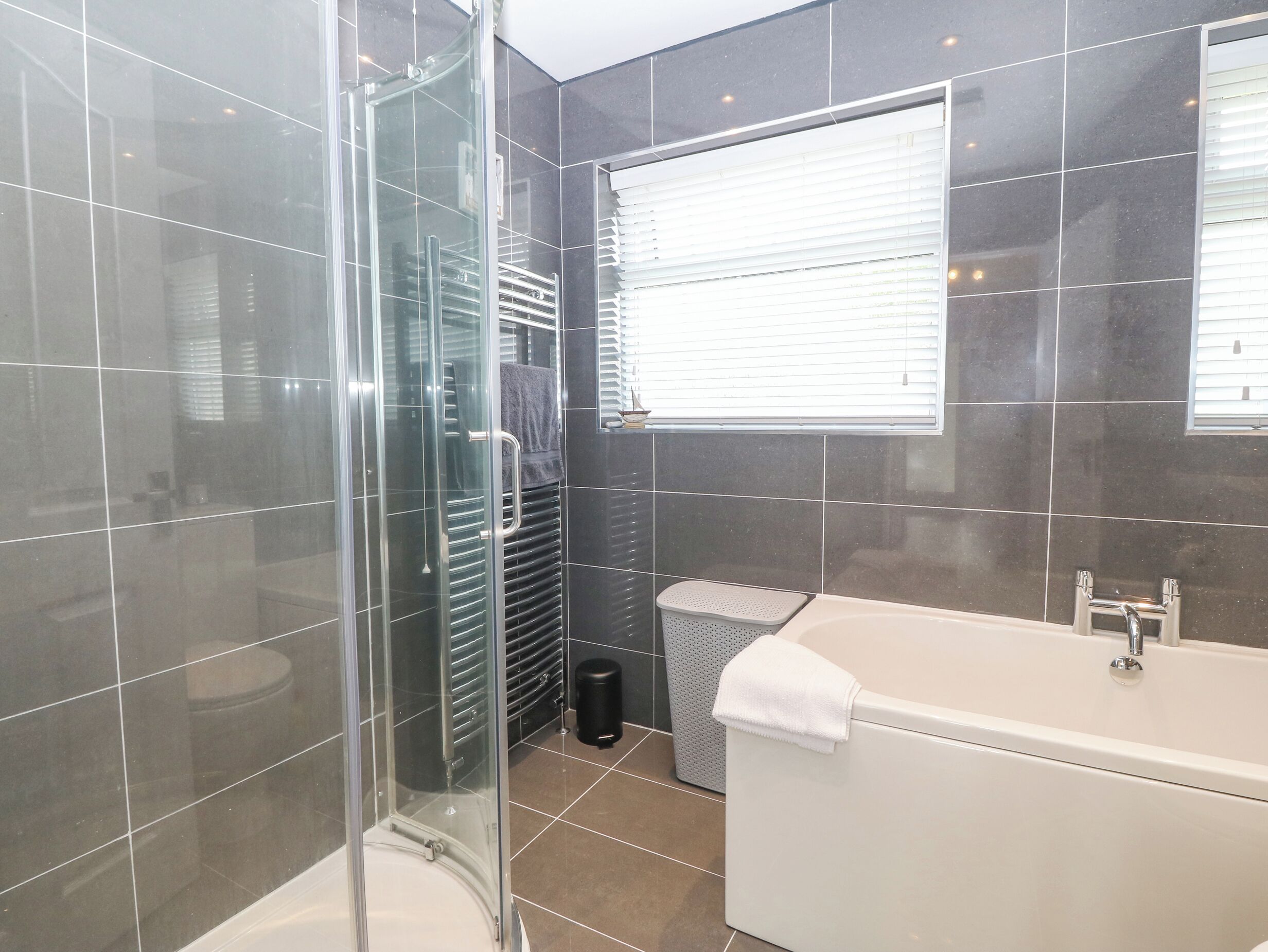 Un baño moderno con cabina de ducha de vidrio, una bañera blanca y una ventana con persianas.