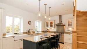 A modern kitchen with a central island, bar stools, and pendant lighting. - Gorphwysfa (Beaumaris)