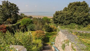 A stone staircase leading to a beach, surrounded by lush greenery and a clear view of the sea. - Gorphwysfa (Beaumaris)