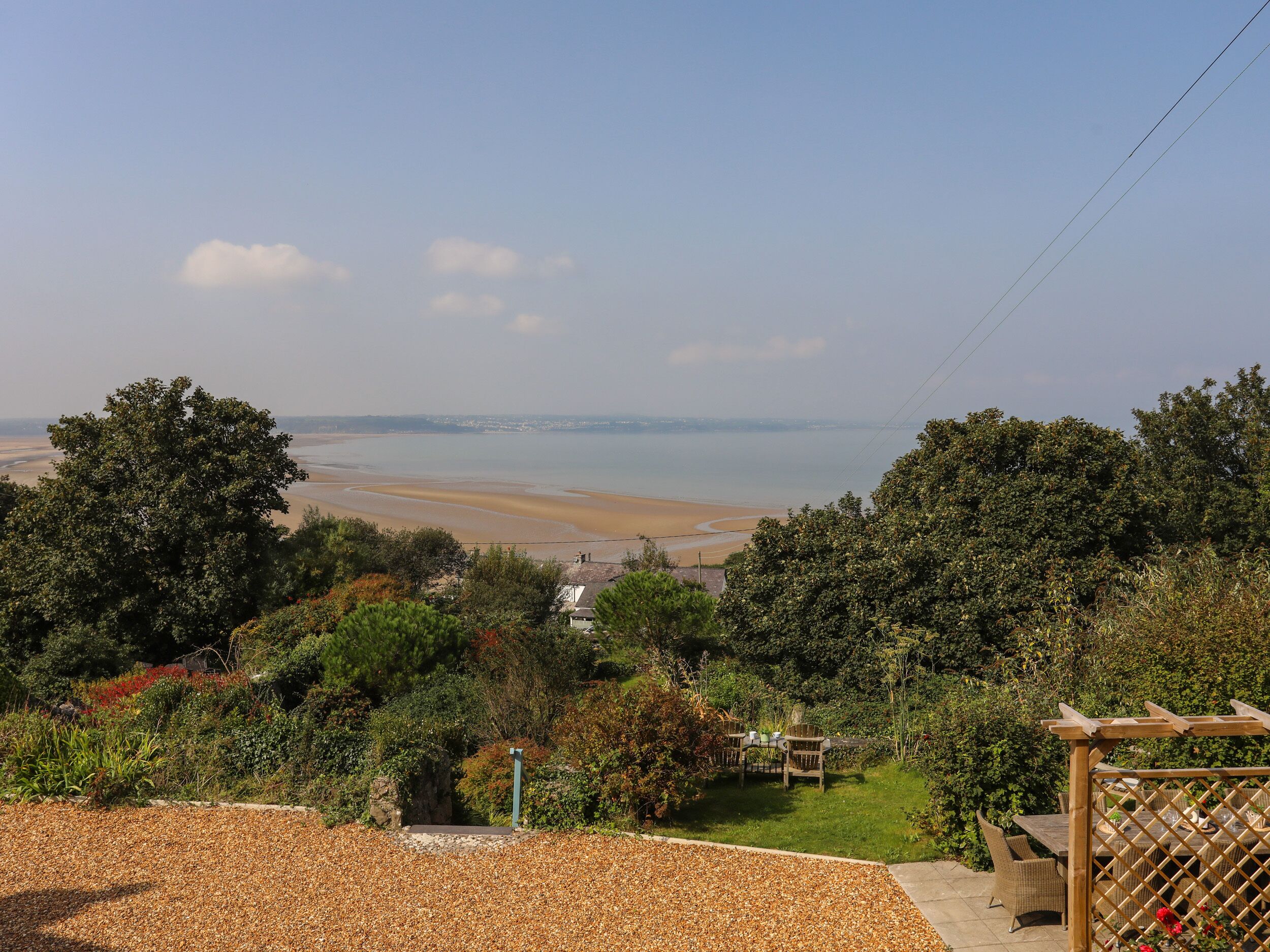 A coastal view with a beach, greenery, and a patio area with outdoor furniture.