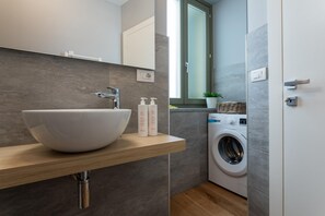 A modern bathroom with a large white sink, a washing machine, and a small shelf with toiletries. - Le Casette del Balon by Wonderful Italy - 2-bedroom Apartment (Turin)
