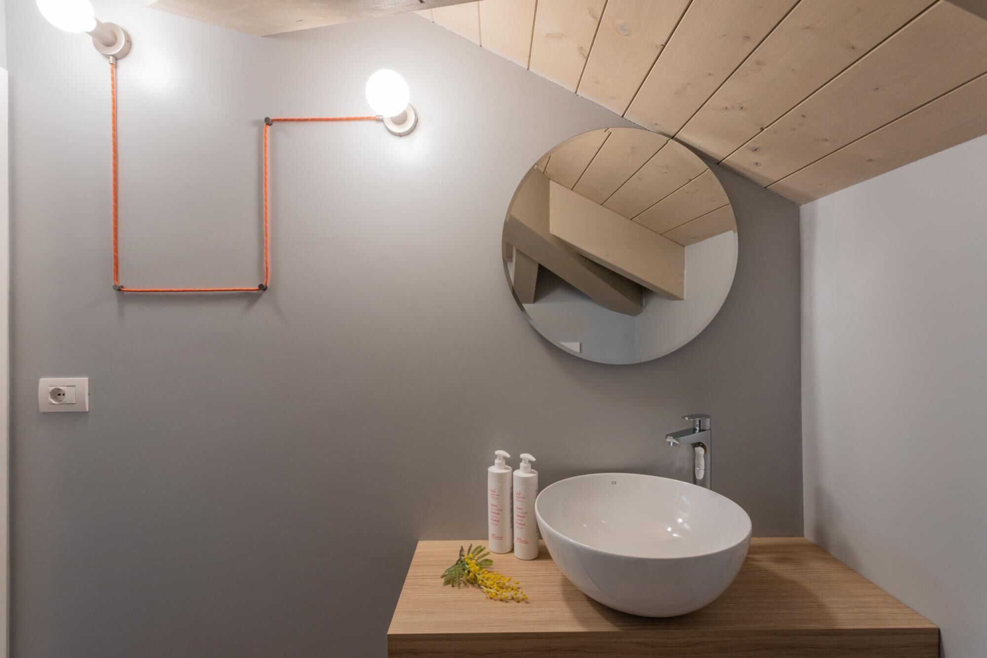 Un baño moderno con un espejo redondo, un lavamanos blanco y un mueble de tocador de madera.