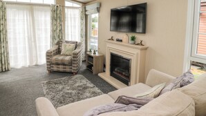 Un salon avec un canapé beige, un fauteuil à motifs, un téléviseur à écran plat, une cheminée et une grande fenêtre avec des rideaux.