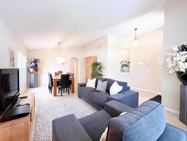 A modern living room with a grey sofa, a dining table with chairs, and a TV on a wooden stand. - Spacious Family Pool Home With Game Room-588ocb 4 Bedroom Home by RedAwning (Davenport)