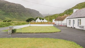 A rural setting with white buildings, a grassy area, and a mountain in the background. - Maghera Caves Cottage (Ardara)