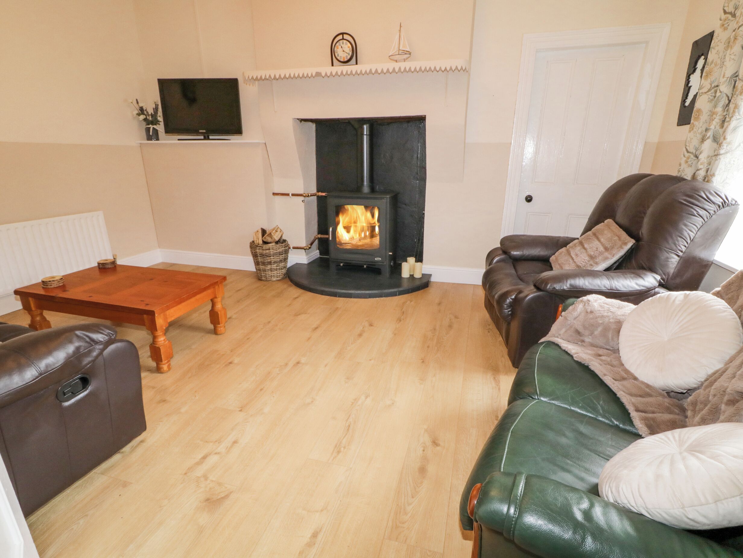 A cozy living room with a fireplace, leather sofas, a wooden coffee table, and a television on the wall.