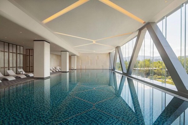 Una piscina interior moderna con diseño geométrico en el techo y vistas al exterior.