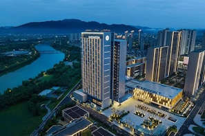 Un hotel Sheraton con diseño moderno, rodeado por un río y montañas al fondo.
