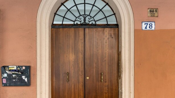 Une porte en bois à deux battants, surmontée d’une arche blanche et d’une fenêtre en verre. Une petite plaque avec le numéro 78 est visible sur le côté droit de la porte.